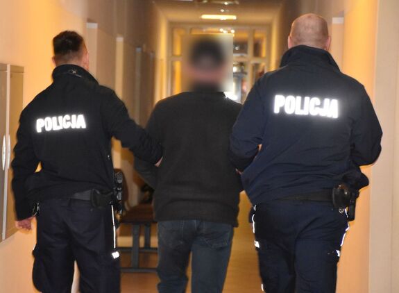 Policjanci prowadzą korytarzem zatrzymanego mężczyznę