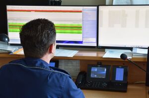 Oficer dyżurny Policji w trakcie służby. Przed policjantem znajdują się monitory.