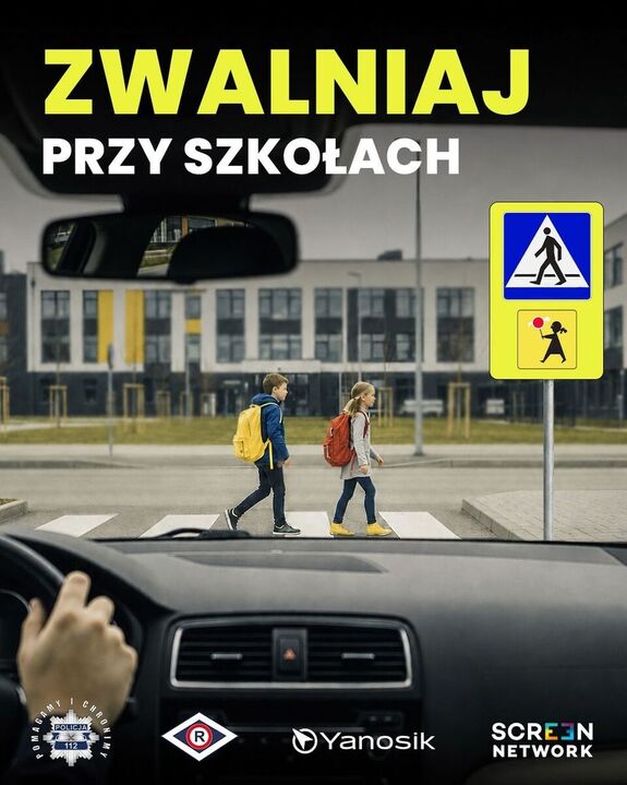 Grafika przedstawia dzieci przechodzące przez przejście dla pieszych, na górze znajduje się napis o treści Zwalniaj przy szkołach. Na pierwszym palnie widnieje osoba kierująca pojazdem.