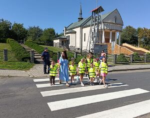 Dzieci w kamizelkach odblaskowych przechodzą przez jezdnię