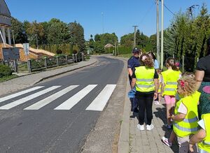 Dzieci w kamizelkach odblaskowych idą chodnikiem