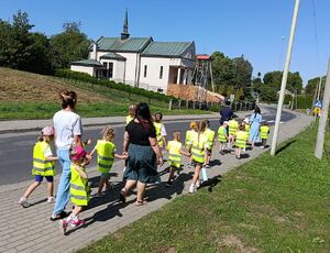 Dzieci w kamizelkach odblaskowych idą chodnikiem
