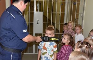 Policjantka z dziećmi przed pomieszczeniem policyjnej izby zatrzymań