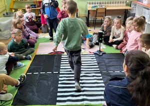 Chłopczyk przechodzi przez pasy w sali lekcyjnej. obok znajdują się dzieci
